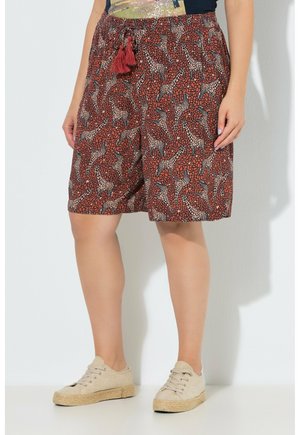 Brązowe szorty do kolan z czerwonymi tasiemkami z frędzlami i nadrukiem żyrafy, noszone z beżowymi butami casual.