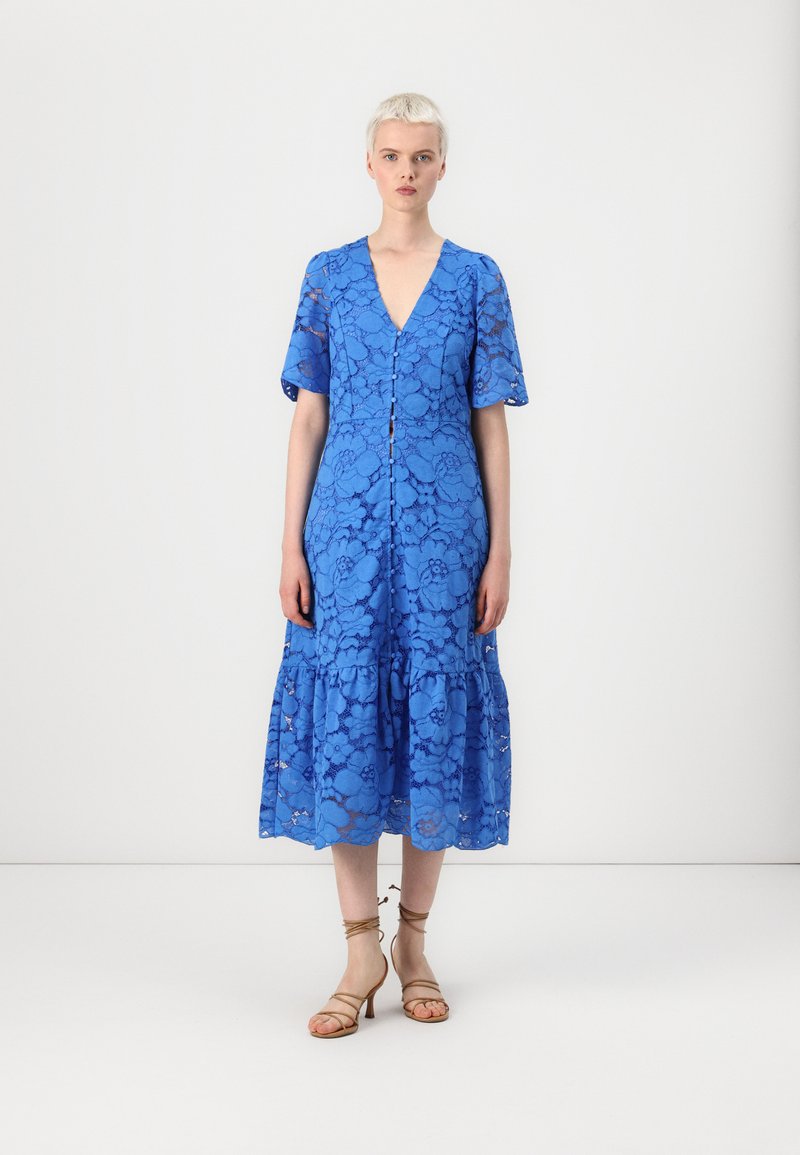 Blue lace midi dress with short, flutter sleeves, a V-neckline, button closure, and a tiered hem. Worn with strappy beige heels.