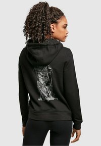Black hoodie featuring a graphic design on the back with a figure, text "La Familia," and a front kangaroo pocket. Smooth fabric texture.