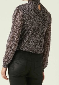 Svart blommig blus med långa ärmar, hög krage och nyckelhålsdetalj på ryggen, tillverkad av lätta tyger med rosa och vita mönster.