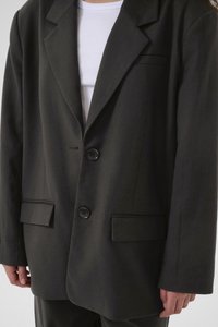Černý blazer se dvěma knoflíky, klopami a předními kapsami. Hladká textura, strukturovaný design a propracovaný střih. Kombinováno s bílým topem.