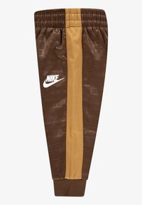Rjave Nike športne hlače z nežno črto, elastičnim manšetom in ponavljajočim se vzorcem besedila "TO STORIŠ" v tkanini.