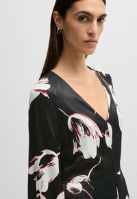 Schwarzes Blumenkleid mit roten und weißen Blumenmustern, tiefem V-Ausschnitt, langen Ärmeln und glatter Satinoberfläche.