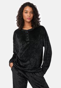 Top negro de velour de manga larga con un patrón texturizado, con un escote con botones y puños negros contrastantes, combinado con pantalones a juego.