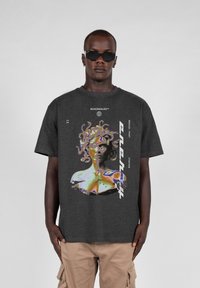 Kortsleeve t-skjorte i kullgrå med et abstrakt grafisk trykk av en figur, med livlige farger og tekstakenter på forsiden.