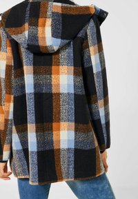 Rutigt huva med svart, orange, blå och grå färger. Tillverkad av texturerad tyg, har en lös passform och framfickor.