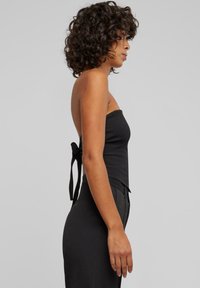 Svart strapless topp med en tettsittende design, med en sløyfeddetalj bak, laget av glatt stoff. Enkel og elegant silhuett.
