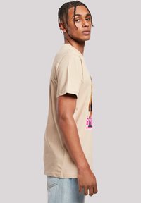 Béžové tričko s krátkým rukávem vyrobené z bavlny, s grafickým potiskem a textem v růžové barvě. Střih je volný s rovním lemem.