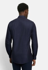 Marineblaue Langarmshirt mit strukturiertem Muster, spitzem Kragen und Knopfmanschetten. Verfügt über einen leicht abgerundeten Saum und eine taillierte Passform.