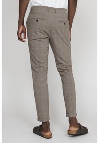 Beiga rutiga byxor med skräddarsydd passform, utrustade med dubbla världfickor och uppvikt nederkant. Bärs med mörka sandaler.