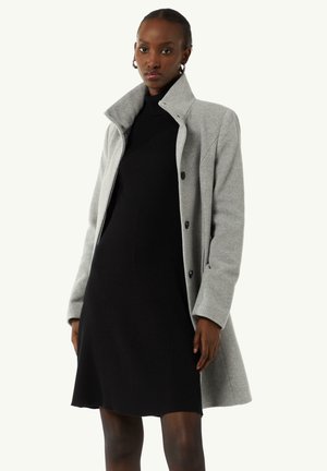 Light grey wool coat with a high collar, button closure, and long sleeves, worn over a black ribbed dress. Smooth texture and tailored design.