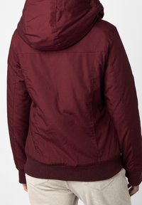 Burgundy huva jacka med en slät textur, ribbad nederkant och axelsömmar. Har en figurnära design och enkel bakdetalj.