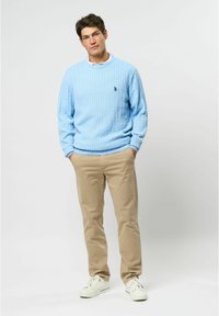 Lichtblauwe kabelgebreide trui met geribde manchetten en zoom, gecombineerd met beige chino's en witte sneakers, met een klein zwart logo.