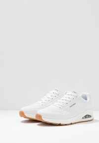 Sneaker blanche avec un design perforé et une semelle en caoutchouc. Dotée d'un coussin d'air visible et d'une subtile marque sur le côté.