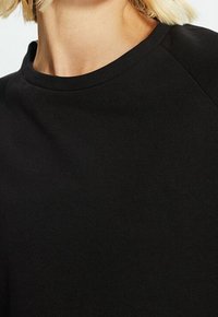 Schwarzer Sweatshirt aus einem glatten, strukturierten Stoff mit rundem Halsausschnitt und Raglanärmel, der ein einfaches und klassisches Design präsentiert.