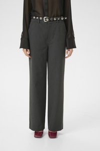 Rechtdoor grijze broek met een gestikte zwarte riem, transparante zwarte blouse met lange mouwen, en rode vierkante schoenen.