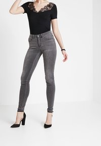 Bodysuit negro con encaje, combinado con jeans gris ajustados que cuentan con una cintura alta y una silueta esbelta, complementado con tacones negros.