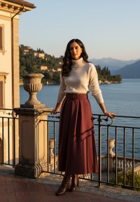 Kremowy prążkowany sweter z golfem i bordowa spódnica w kształcie litery A z paskiem. Modelka stoi przy balustradzie, ma na sobie brązowe botki o gładkiej fakturze.