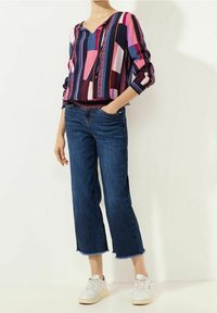 Multicolored long-sleeve blouse with geometric patterns, paired with blue cropped jeans and white sneakers. Features a relaxed fit and V-neck.