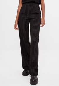 Höga svarta byxor med vita ränder, veckad front och vida ben. Tillverkade av ett mjukt tyg med en subtil glans.