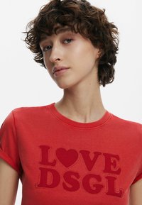 T-shirt rossa a maniche corte in cotone con la scritta "I LOVE DSGL" accompagnata da un cuore, decorata con piccole borchie per un tocco di stile.