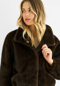 Brown faux fur coat with a wide collar, button closure, and soft texture, capturing light from various angles.