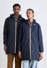Les vestes à capuche bleu marine sont dotées d'une fermeture éclaire à l'avant avec des rayures jaunes et blanches, des poignets élastiques et une coupe décontractée. Les modèles portent des pantalons contrastants.