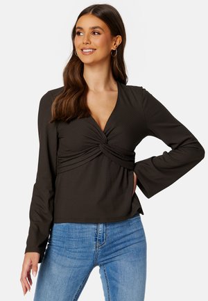 Dunkel gestreiftes Langarmoberteil mit tiefem V-Ausschnitt und gedrehtem Frontdesign, kombiniert mit hellblauen Jeans.