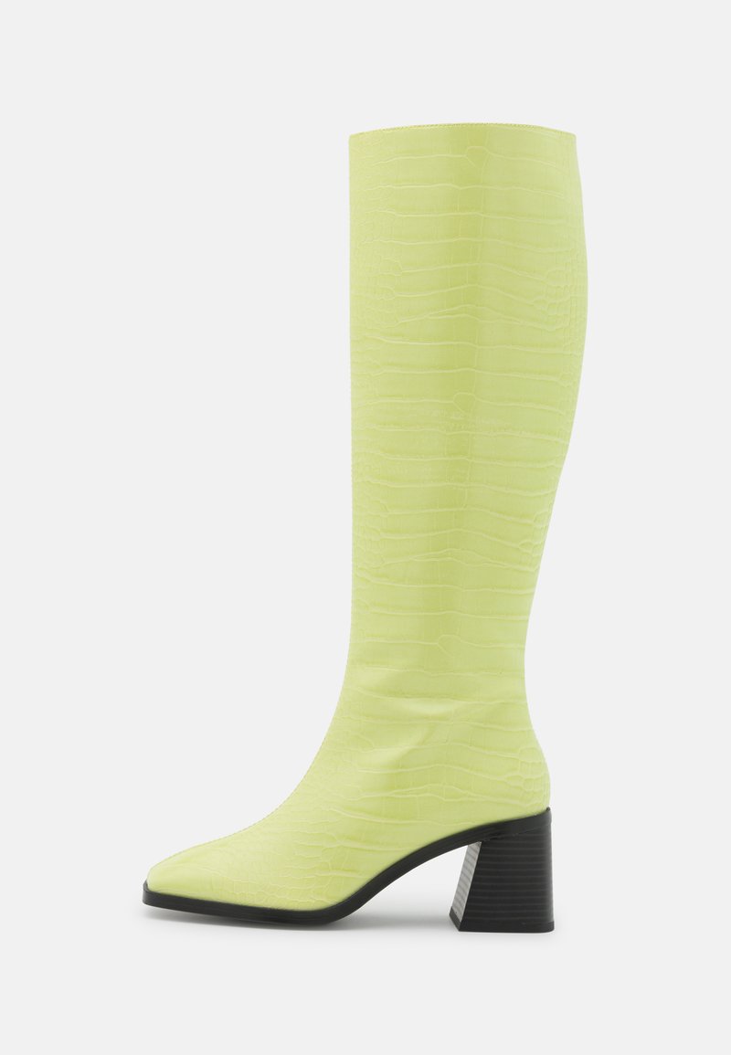 Bota até ao joelho em amarelo com relevo de crocodilo, com bico fino e um salto bloco preto texturizado. Acabamento liso e brilhante com um design ajustado.