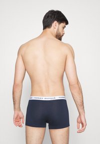 Boxer-briefs navy avec une ceinture blanche arborant le logo "TOMMY HILFIGER". Tissu doux et coupe ajustée, visible depuis l'arrière.