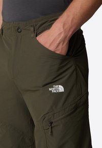 Oliivinvihreät vaellushousut, joissa on sileä pinta, vetoketjullinen tasku ja The North Face -logo valkoisena vasemmassa reisissä.