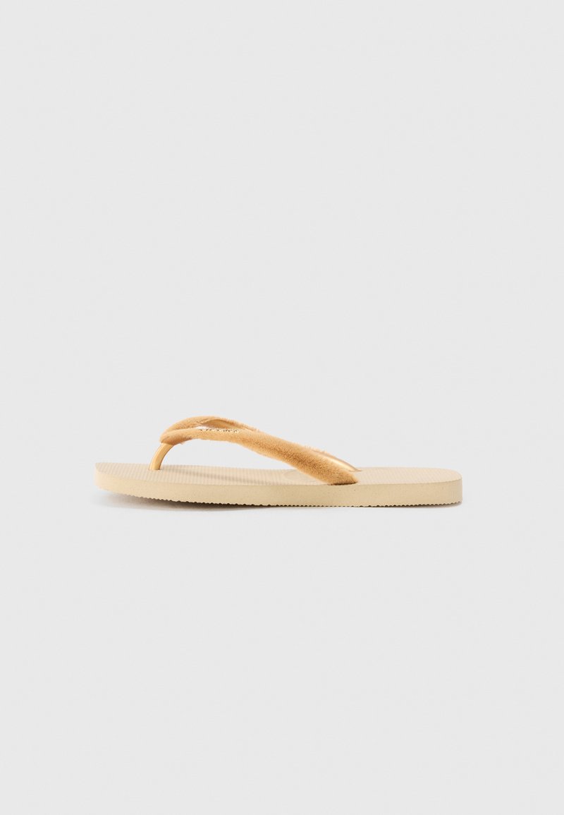 Infradito color tan con una fascia morbida e texturizzata e una suola in gomma beige. Presenta un design liscio e piatto con dettagli rigati sulla suola.