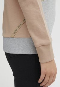 Light pink and gray sweatshirt with ribbed cuffs, featuring a side logo tag. Soft cotton blend material; structured and relaxed fit.