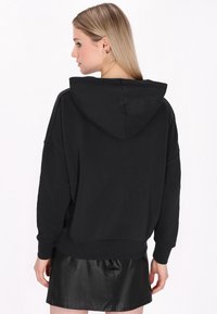Sudadera negra de gran tamaño en mezcla de algodón, con capucha, hombros caídos, puños y dobladillo de canalé. Combinada con una mini falda de efecto piel negra.