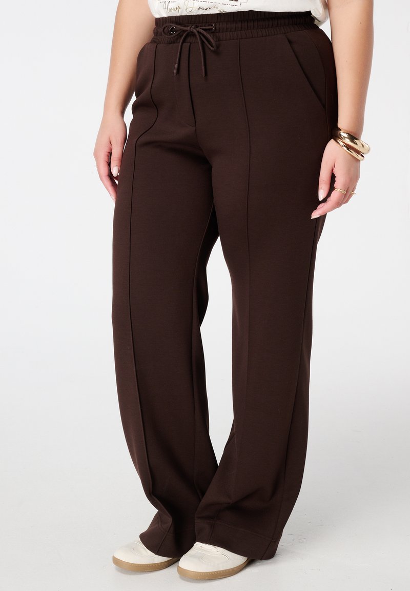 Bruine wijde broek van zacht materiaal, met een elastische tailleband en trekkoord, en zijzakken voor extra gemak.