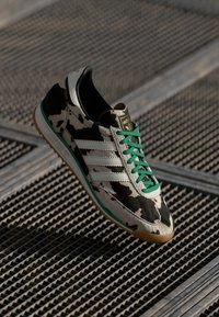 Cow print sneaker with a textured leather upper, green laces, three white stripes, and a gum rubber sole. Accented with a gold logo patch.