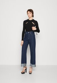 Top negro de manga larga acanalado con detalles recortados, combinado con jeans oscuros de tiro alto con dobladillos y sandalias negras de tacón.