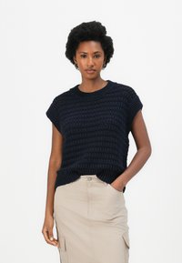 Marineblauer Strickpullover mit einem strukturierten Muster und kurzen Ärmeln, kombiniert mit einem beige knielangen Rock mit Seitentaschen.