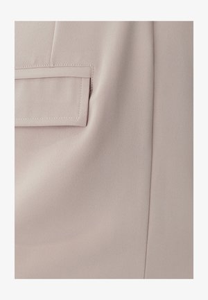 Una tela de color rosa claro con una textura fina presenta un pequeño bolsillo diagonal y costuras visibles. El material parece suave y elegante.