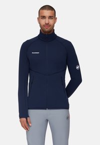 Marine kleur fleece jack met een hoge kraag, ritssluitingen en contrasterende stiksels. Voorzien van een logo op de borst en een embleem op de mouw.