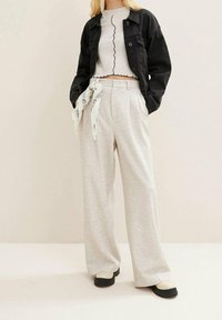 Czarna kurtka dżinsowa, szary prążkowany top typu crop z falbaniastymi krawędziami, jasnoszare spodnie szerokie z dekoracyjnym szalem oraz czarne platformy.