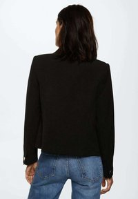 Czarna marynarka dopasowana z długimi rękawami, mankietami na jeden guzik i gładką teksturą; zestawiona z jasnoniebieskimi dżinsami.