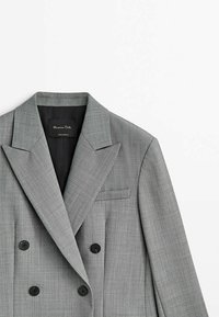 Blazer grigio doppiopetto realizzato in tessuto texturizzato. Presenta un colletto a rever, due bottoni neri e una tasca sul petto.