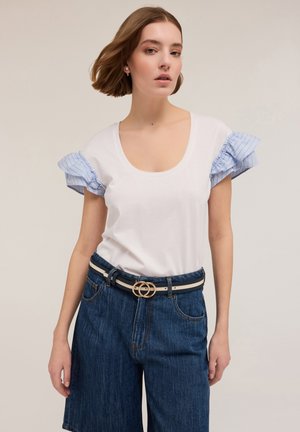 Witte katoenen t-shirt met blauw gestreepte ruffles op de mouwen, gecombineerd met hoge denim shorts en een bicolor riem met een ronde gesp.