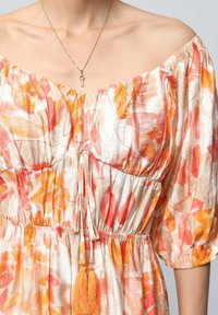 Robe florale décolleté en tissu doux, présentant des tons orange et pêche, taille froncée et accents à pompons.