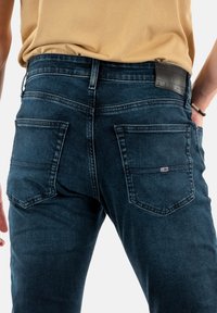 Jeans de mezclilla azul oscuro con una textura ligeramente desgastada, que cuentan con dos bolsillos traseros, un parche de cuero con la marca y detalles de costura tradicionales.