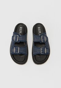 Sandali slide in denim blu con borchie argentate, due cinturini regolabili e suola in gomma nera. Presentano una soletta con marchio.