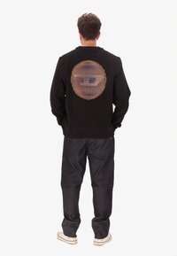 Felpa nera con un grande motivo a pois multicolori sul retro. Abbinata a pantaloni in denim scuro e sneakers bianche.