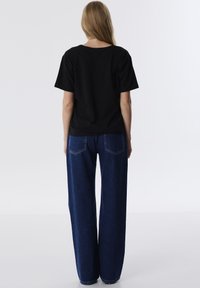 Zwart shirt met korte mouwen gecombineerd met losse blauwe denim jeans, met een rechte pijp en achterzakken met gebogen naden.