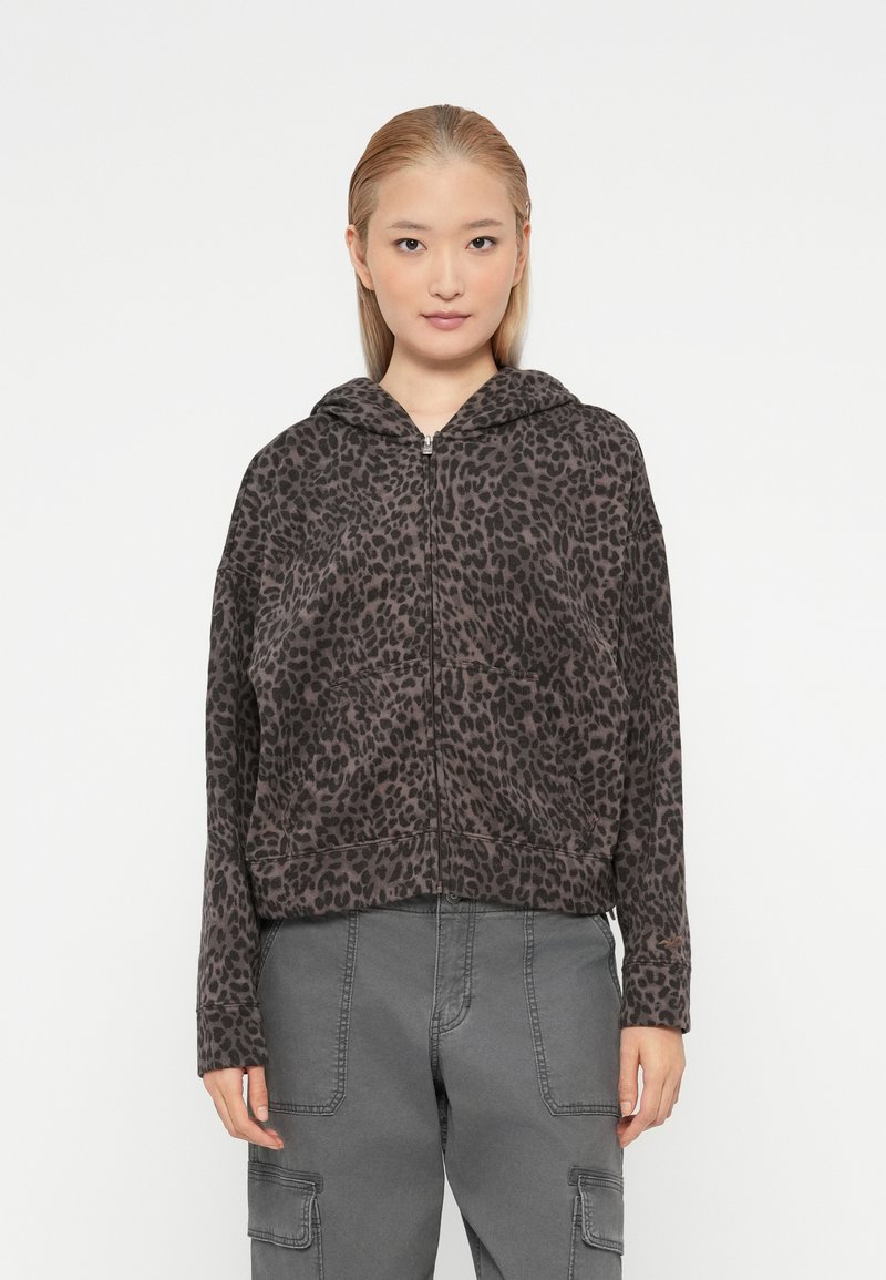 Hoodie cinzento com padrão de leopardos, feito de um tecido suave, apresentando um fecho de correr na frente, capuz com cordão e mangas longas. Estilizado com calças cargo cinzentas.